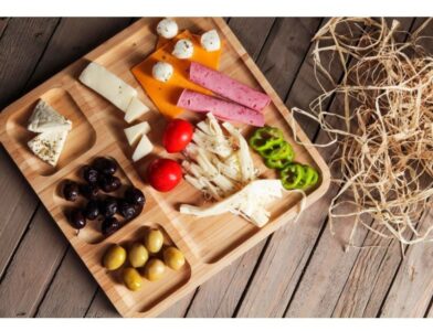A 4 Compartment Bamboo Serving Tray with a variety of cheeses, olives, and meats.