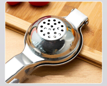 A stainless steel small fruit juicer on top of a wooden cutting board.