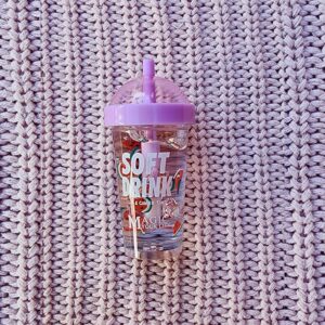 A pink cup with a straw sitting on top of a knitted blanket.