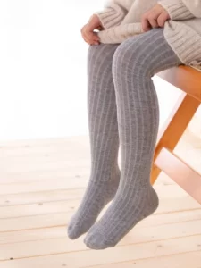 A girl sitting on a wooden chair wearing Solid Color Boy Girl Baby Tights.