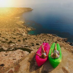 Two women sitting on Outdoor Inflatable Recliners on a cliff overlooking the ocean.