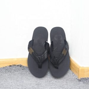 A pair of black flip flops against a white wall.