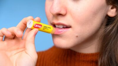 A woman is holding a tube of Carmex Strawberry Lip Balm.