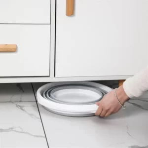 A person putting a Plastic Folding Bucket under a kitchen cabinet.