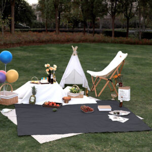 A solid color picnic out door blanket is set up in a grassy area.