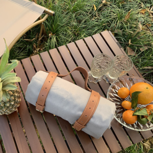 A solid color picnic out door blanket on a wooden table with oranges and pineapples.